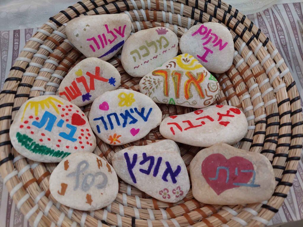 קערה עשויה מקש ובתוכה אבנים מאוירות שרשומות עליהן מילים כמו: אושר, בית, אומץ, כסף, אור, מלכה, שלווה, מקום ראשון ואהבה